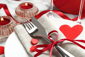 Romantic place setting for Valentine's day. Plate with cutlery, candles and decorative hearts on white table, closeup