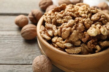 Peeled walnuts in bowl and whole ones on wooden table, closeup. Space for text