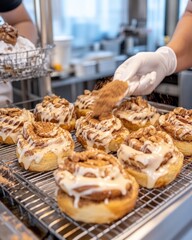 Cinnamon Rolls Being Prepared And Sprinkled With Cinnamon Powdering Sugar And Glazeings on Wire Racks Ready For Display In A Bakery Kitchen Setting With Golden Topping on Top of Doughy Rolls and