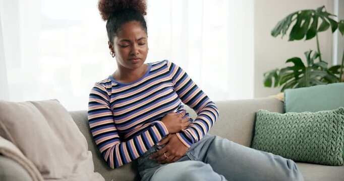 Sick, home and woman with stomach ache, pain or period cramps with medical emergency on sofa. Diarrhea, constipation and African person with problem, digestion or gut health with appendicitis disease