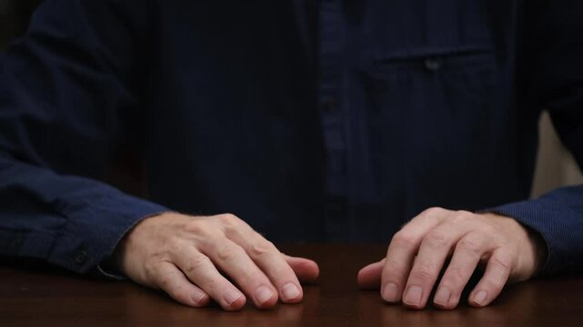 businessman in a blue shirt sits at a table and gestures with his hands, explaining and proving his opinion. hands in close-up. front view.