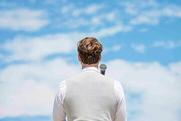 Fototapeta premium A man in formal attire stands with his back to the camera, gazing at a clear blue sky filled with soft clouds.