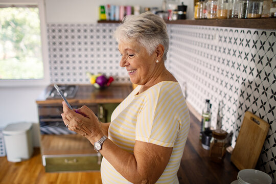 Smiling senior woman using smartphone in modern kitchen