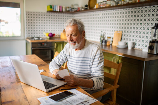 Senior man managing finances online with laptop at home