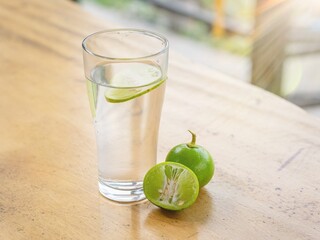 Lifestyle Health Care Concept. A glass of water with lemon inside and a fresh green lime on the wooden table. Warm water mixed with lemon, fruits that help nourish the body. Digestive drinks detox 