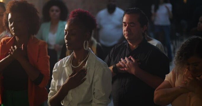 Congregation worshipping with hands on heart during evangelical church gathering, African descent preacher delivering inspiring message, spiritual unity and devotion