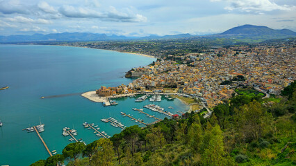 view of a coastal city with a harbor and yachts surrounded by mountains and green hills. Among the Mediterranean architecture, turquoise sea and cozy atmosphere. Italy, Sicily
