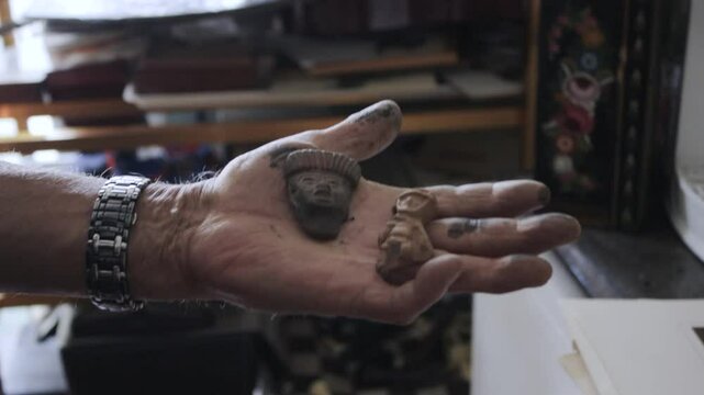 Mano de hombre mexicano sosteniendo unas figurillas de barro artesanales. 