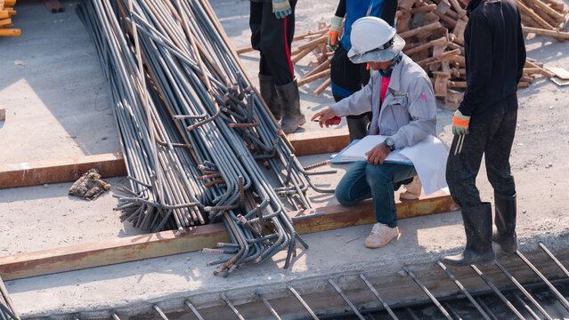Construction Site Coordination, Workers at construction site inspect steel rebar materials while discussing project details to ensure safety and quality standards are met during build