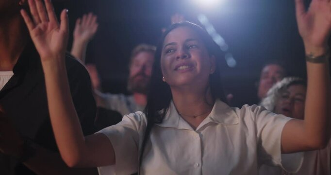 Woman raising hands in spiritual praise during evangelical worship service, joyful expression, white shirt, diverse congregation with hands lifted in celebration of faith