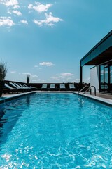 Fototapeta premium Rooftop pool with blue water, lounge chairs, building, blue sky and white clouds