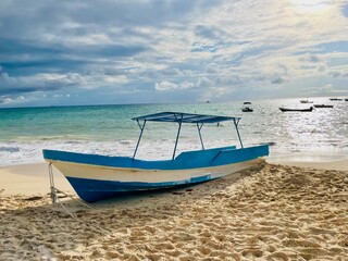 Fototapeta premium Traditional Wooden Fishing Boat on a Sandy Beach with a Scenic Ocean View in Playa Del Carmen Mexico - concept of travel, holiday, rustic