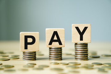 Wooden blocks with the letters PAY stacked on piles of coins representing salary payment, financial transactions, payroll management, business expenses, economic exchange, and monetary flow
