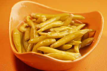Green chili peppers in vibrant orange bowl on bright table