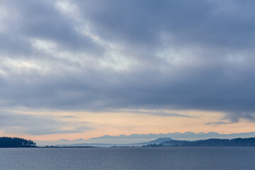 Overcast Sky Over Tranquil Waterfront with Distant Mountains and Forest