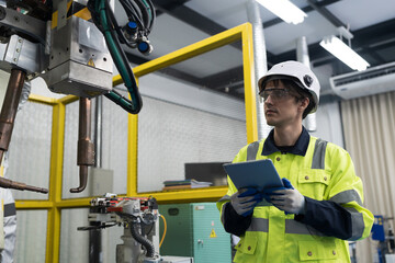 Male engineer using digital tablet control automatic robotic hand machine welding in building room...