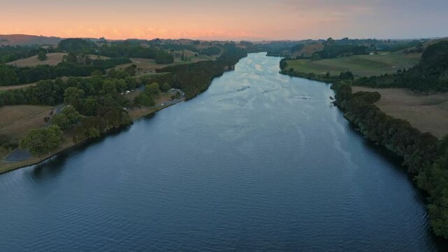 Tranquil river at sunset, with gentle ripples and small boats. Scenic countryside surrounds the waterway. Waikato River, Karapiro, Waikato, New Zealand