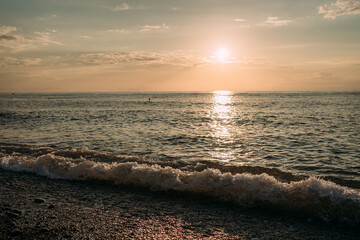 Sunset over the Black Sea in Batumi, with golden light reflecting on the waves. Gentle ripples and silhouettes of swimmers create a serene seascape, while clouds add depth to the dramatic evening sky