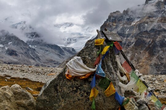 Colorful Tibetan prayer flags flutter against the rugged backdrop of Kanchenjunga Base Camp in the Nepalese Himalayas, symbolizing peace and spirituality amidst the towering peaks.