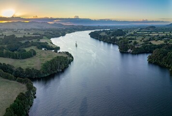 Aerial view of a Waikato River winding through farmland at sunset. Tranquil scene with a small boat on the water.  Karapiro, Waikato, New Zealand