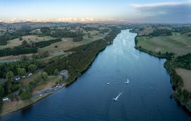Fototapeta premium Aerial view of Waikato River winding through a rural landscape. Motorboats and a kayak are on the water, while campers are parked along the riverbank. . Karapiro, Waikato, New Zealand