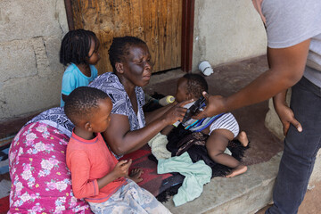 African village, NGO charity social worker using a phone, showing family with three children the...