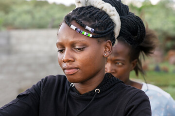 African village, portrait single African teenager girl with braids standing in the yard , front of a house, challenges of poverty in rural communities, reflecting the need for humanitarian aid