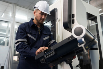 Male engineer control CNC machine from monitor in factory. Male factory worker working with lathe...