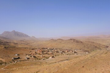 Expansive desert landscape with a small village under clear blue skies in Morocco during midday