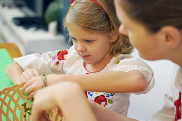 Obraz premium Mother and daughter at the table in traditional Ukrainian costumes weaving a basket for Easter