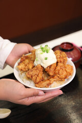 A plate of crispy fried chicken topped with creamy sauce and green onions, held by a person against a simple background.