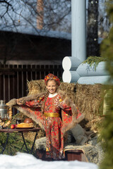 A blonde girl in a national Russian costume on the Maslenitsa holiday. A beautiful russian girl in a national costume made of a fur cape and kokoshnik on the background of a hayloft. 