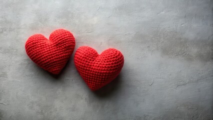 Obraz premium Two lovingly crafted red crocheted hearts rest gently on a textured grey surface.