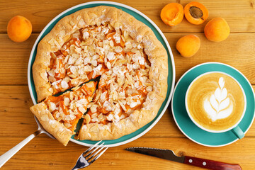 Homemade pie galette with apricots and cup of coffee cappuccino on wooden table. Top view.