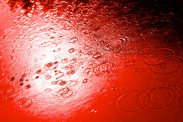Red ocean bloody water drops background with blue sky reflection and blood circles on dark asphalt. Murder and killing. War crime. Close up.