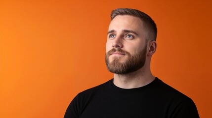 Obraz premium Contemplative man in black against orange background. Ideal for modern portraiture, minimalist style, and personal reflection content.