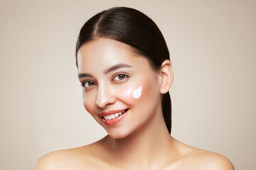 Beautiful young woman applying cosmetic cream treatment on her face isolated on background . Girl...