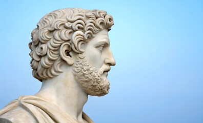 A classical Greek marble bust of a bearded man with curly hair, elegantly isolated against a light blue background. The composition allows for copy space.
