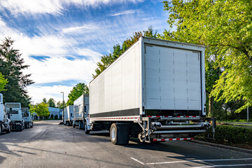Middle duty day cab big rig semi trucks with box trailers and lifting platform in the back standing...