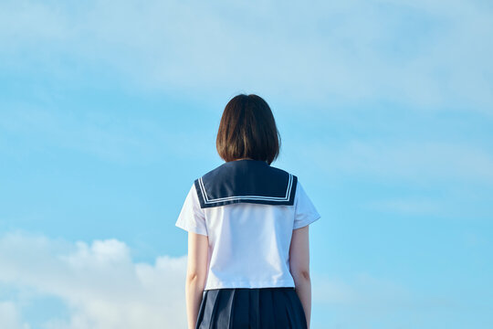 青空と海を背景に立つ女子高校生