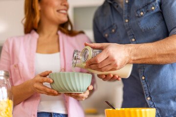 couple is making cereal for breakfast together in the kitchen, preparing a bowl of cereal and pouring milk. Warm and loving moment, togetherness and shared morning routines in a cozy home setting.