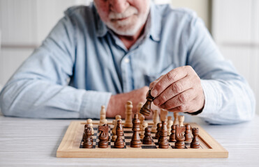 Close up on chess board and hands of senior man playing alone with chess on wooden table. Pastime...