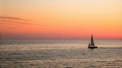 Fototapeta premium Ocean sunset with sailboat on horizon, serene landscape, warm light, blue sky