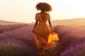 Obraz premium Barefoot woman wearing orange dress walking in lavender field at sunset enjoying freedom and nature