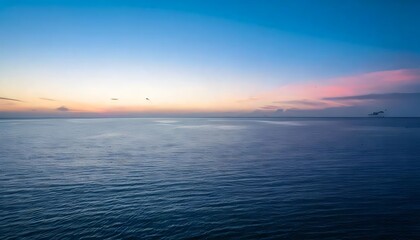 Naklejka premium A vast, empty ocean under a soft pink and blue sunset sky, where the water and sky blend sea