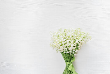 delicate bouquet of lily of the valley flowers with lush green stems placed on a white wooden surface, creating a soft and elegant spring composition