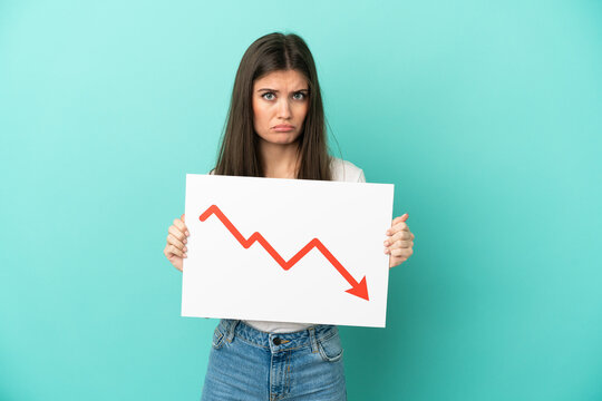 Young caucasian woman isolated on blue background holding a sign with a decreasing statistics arrow symbol with sad expression