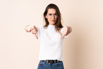 Young woman over isolated beige background showing thumb down with two hands