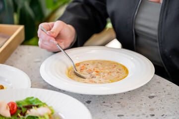 A close-up of a person enjoying a bowl of creamy soup, garnished with vegetables, on a stylish table setting. Fresh salad and additional dishes are visible, creating a cozy dining atmosphere.