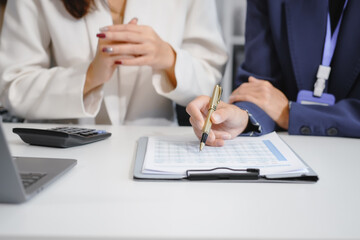 Obraz premium Two Asian female business woman sit desk,discussing business investments.They analyze financial data, explore market opportunities, and strategic growth to maximize returns ensure business success